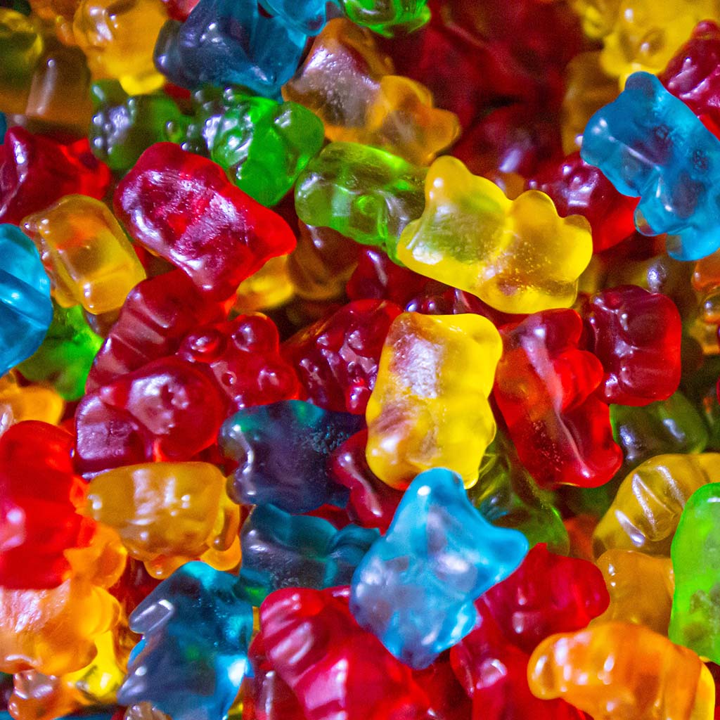 Closeup shot of pile of shiny, colourful gummy bears; because the gummy bears are translucent, it looks like exquisite stained glass art.