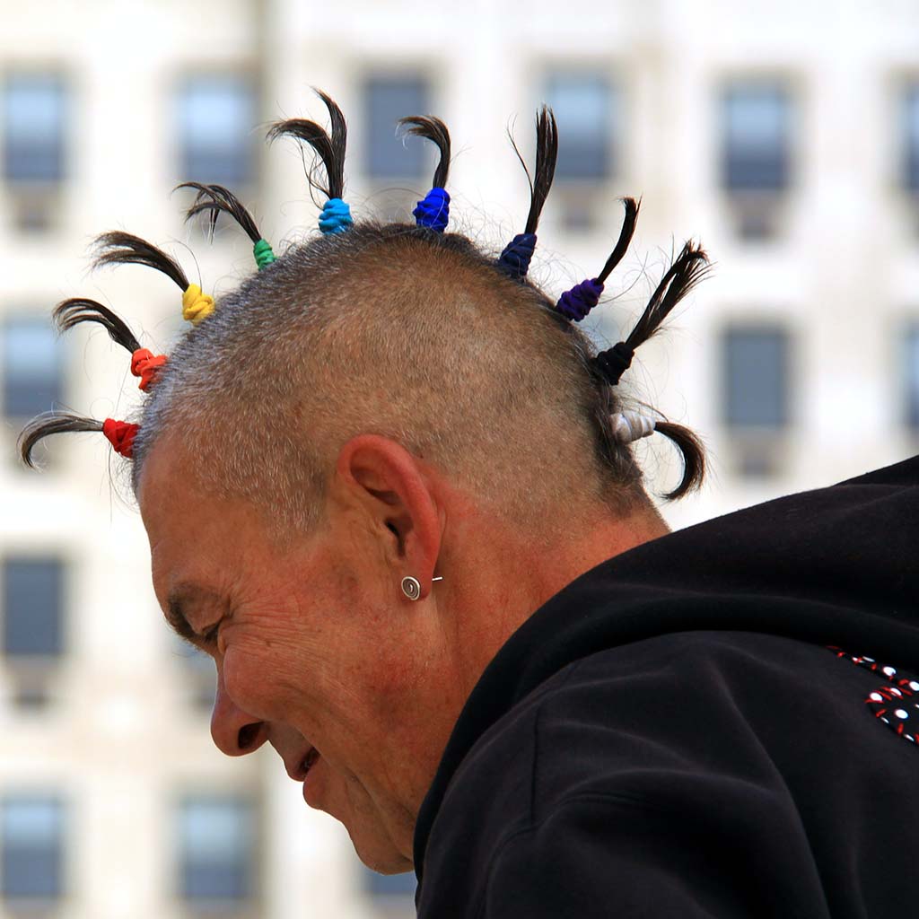 Profile view of a smiling person with a cool mohawk wears rainbow hair bands to make mohawk spikes.