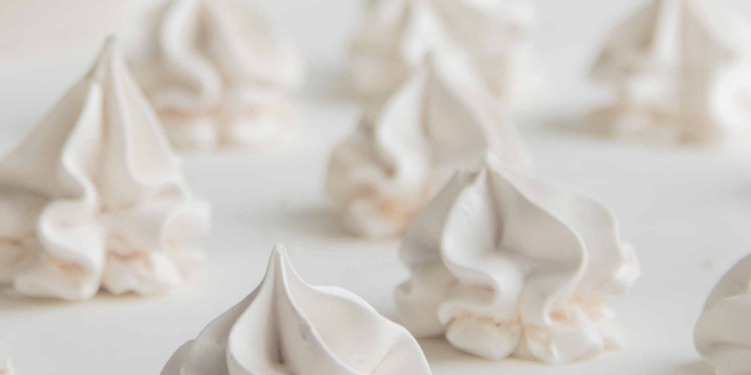 Closeup shot of gorgeously piped fluffy white meringues against a white background