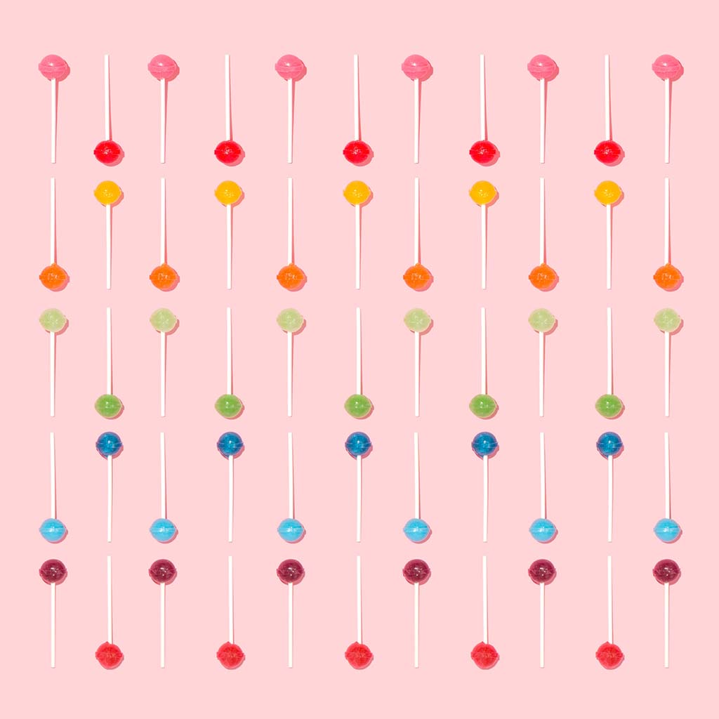 Colourful lollipops are arranged neatly against a peach-coloured background