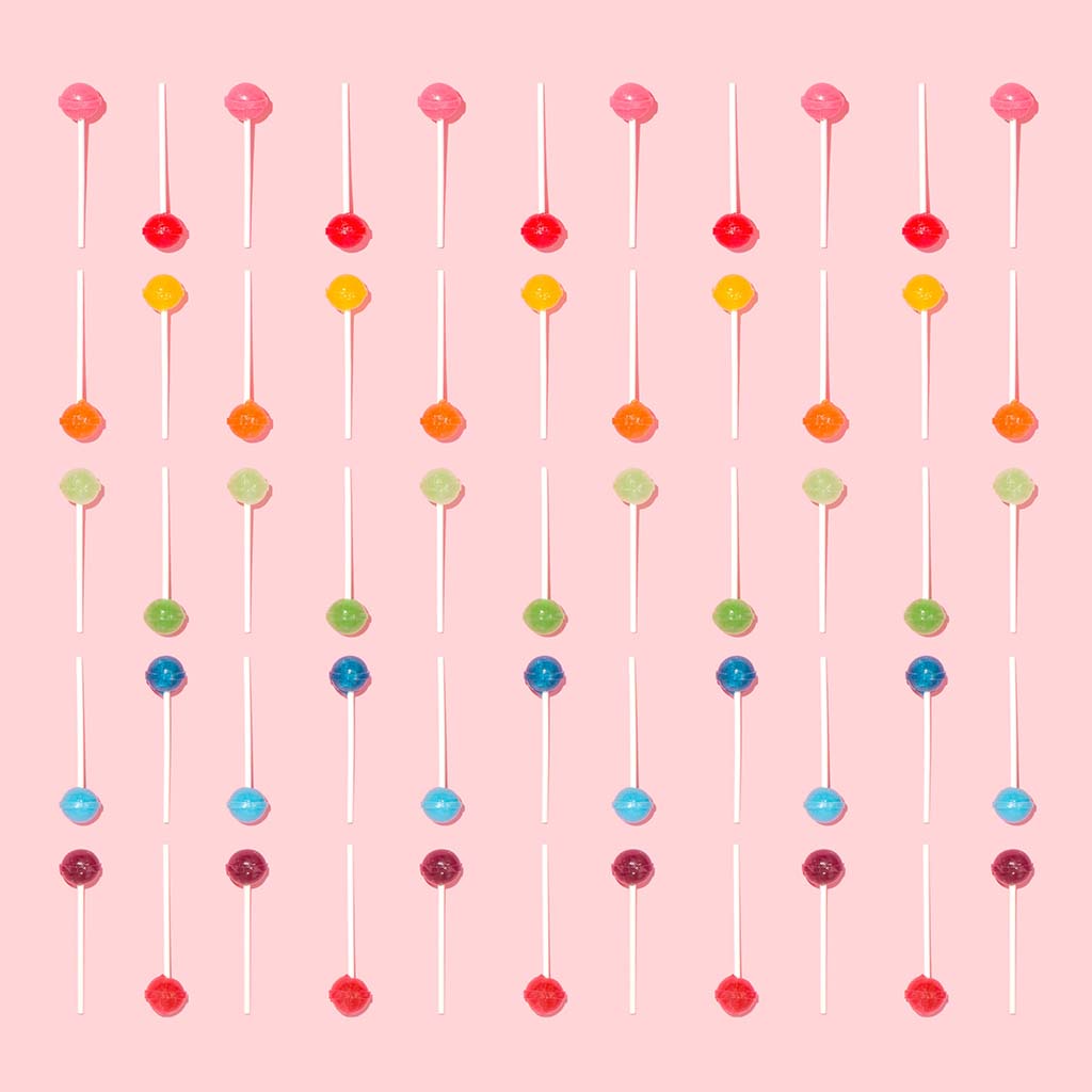 Colourful lollipops are arranged neatly against a peach-coloured background