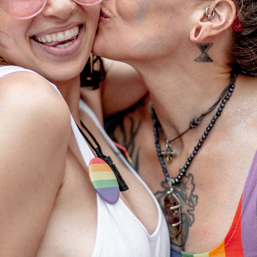 Closeup shot of a beautiful lesbian couple smiling and kissing on the cheek at a gay pride event.